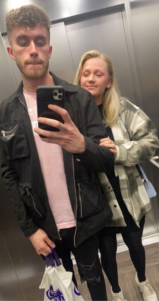 Rhianna poses behind her boyfriend who takes a selfie while in a lift