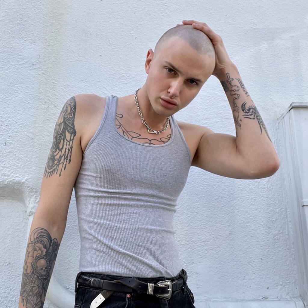 Kyle poses with chains and a grey vest top.