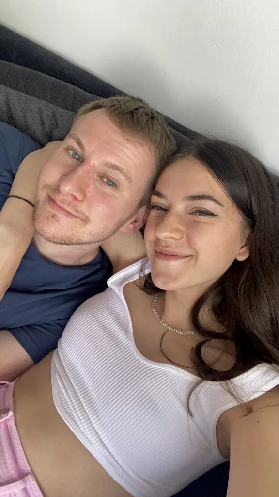Olivia and her partner smile while on the sofa. 