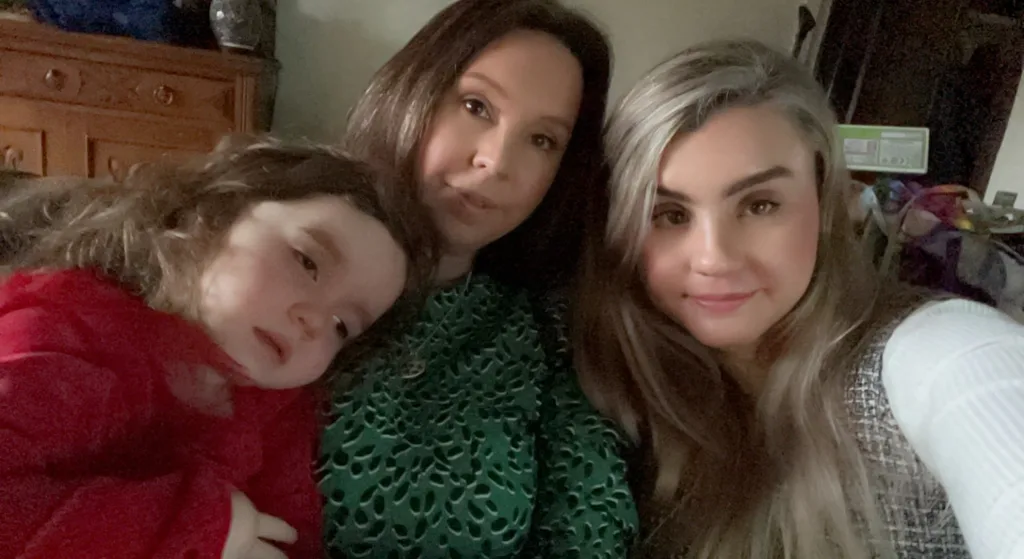 Lisa poses in a green top next to Imogen in a red jumper and her other daughter who is wearing a white jumper. 