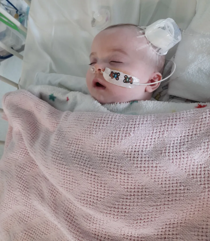Iris-Rose is pictured in hospital with a blanket over her and wires attached to her body. 