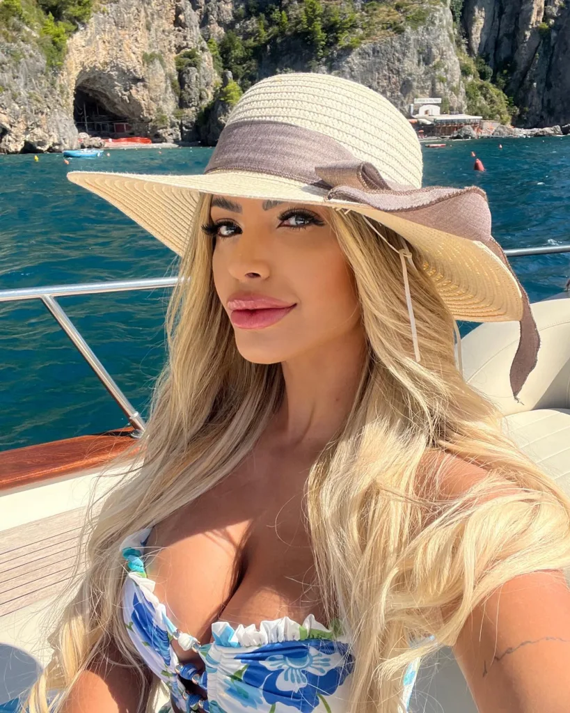 The model poses while on a boat wearing a blue bikini top and sun hat. 