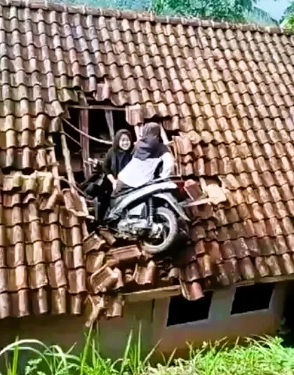 A motorcycle crash in Indonesia leaves two women stuck on a roof, sparking online speculation about repair costs and rooftop parking jokes.
