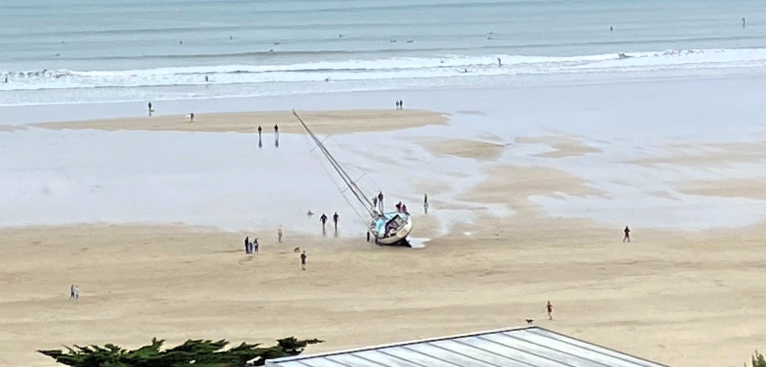 Yacht runs aground on Polzeath beach, Cornwall, after skipper's reported ‘wrong turn’; coastguard and lifeboats assist as onlookers watch from a safe distance.
