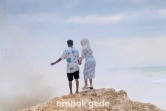 A couple's romantic selfie took a dramatic turn when a huge wave knocked them off a rock in Indonesia - sending them plunging to the beach in a washed-out surprise.