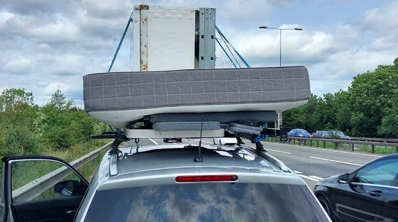 A driver was stopped on the M11 with a fridge, mattress, and picnic table roped to their car roof, prompting police warnings and shocked reactions over the dangerous setup.
