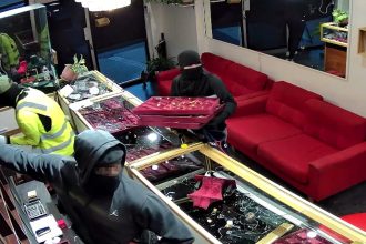 A violent Brisbane jewellery heist left shop owner Bijay Sunar hospitalised and £47,000 in gold stolen. Police released CCTV as a manhunt continues for the four masked thieves.