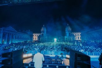 Image of artist standing at the decks in front of a crowd at Old Royal Naval College during Labyrinth on the Thames music series with a blue light