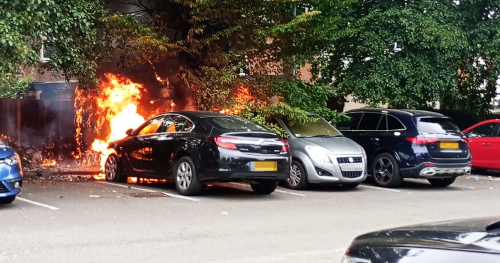 A black Vauxhall Insignia burst into flames in a Birmingham car park, spreading to fencing and nearby vehicles before firefighters quickly extinguished the engine blaze.