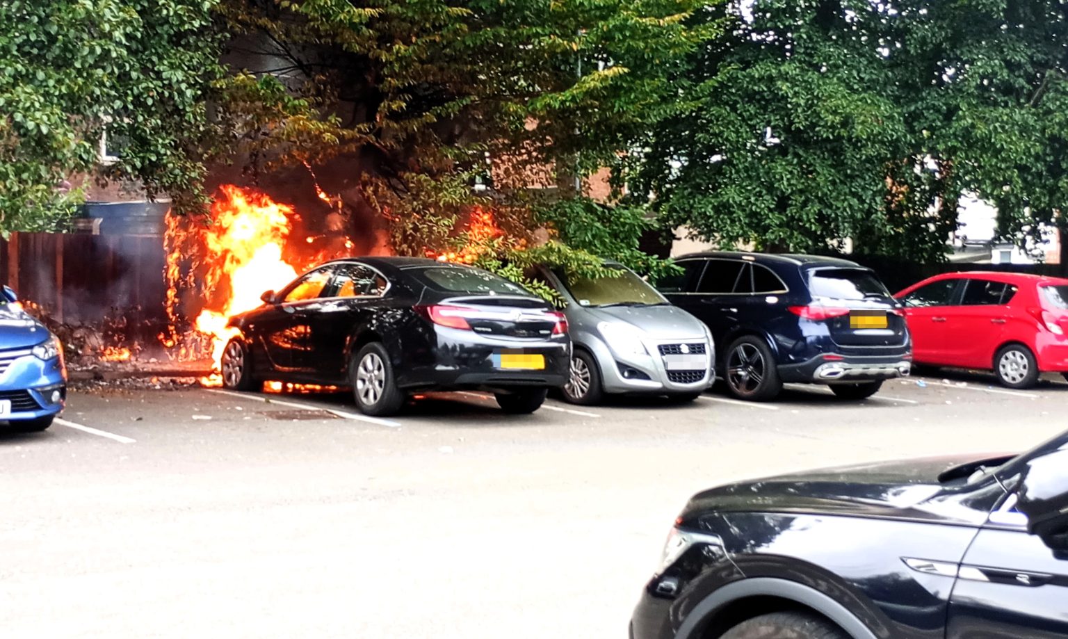 A black Vauxhall Insignia burst into flames in a Birmingham car park, spreading to fencing and nearby vehicles before firefighters quickly extinguished the engine blaze.