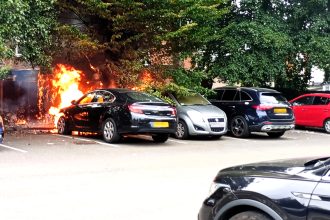 A black Vauxhall Insignia burst into flames in a Birmingham car park, spreading to fencing and nearby vehicles before firefighters quickly extinguished the engine blaze.