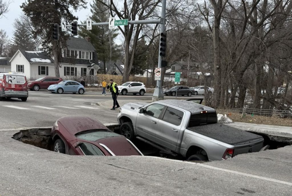 Two cars swallowed by horror sinkhole after road collapses in Omaha - drivers forced to climb out of deep shaft as SUV nearly disappears into the ground.