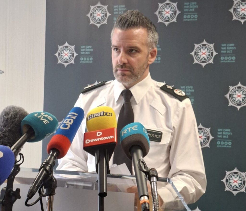 A car bomb exploded yards from a police officer outside a Belfast station after a delivery driver was forced at gunpoint to transport the device, with families narrowly escaping injury.