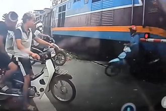 A distracted biker on his phone narrowly survived being clipped by a 14-carriage train in Hanoi after riding around a lowered level crossing barrier in a terrifying near miss.