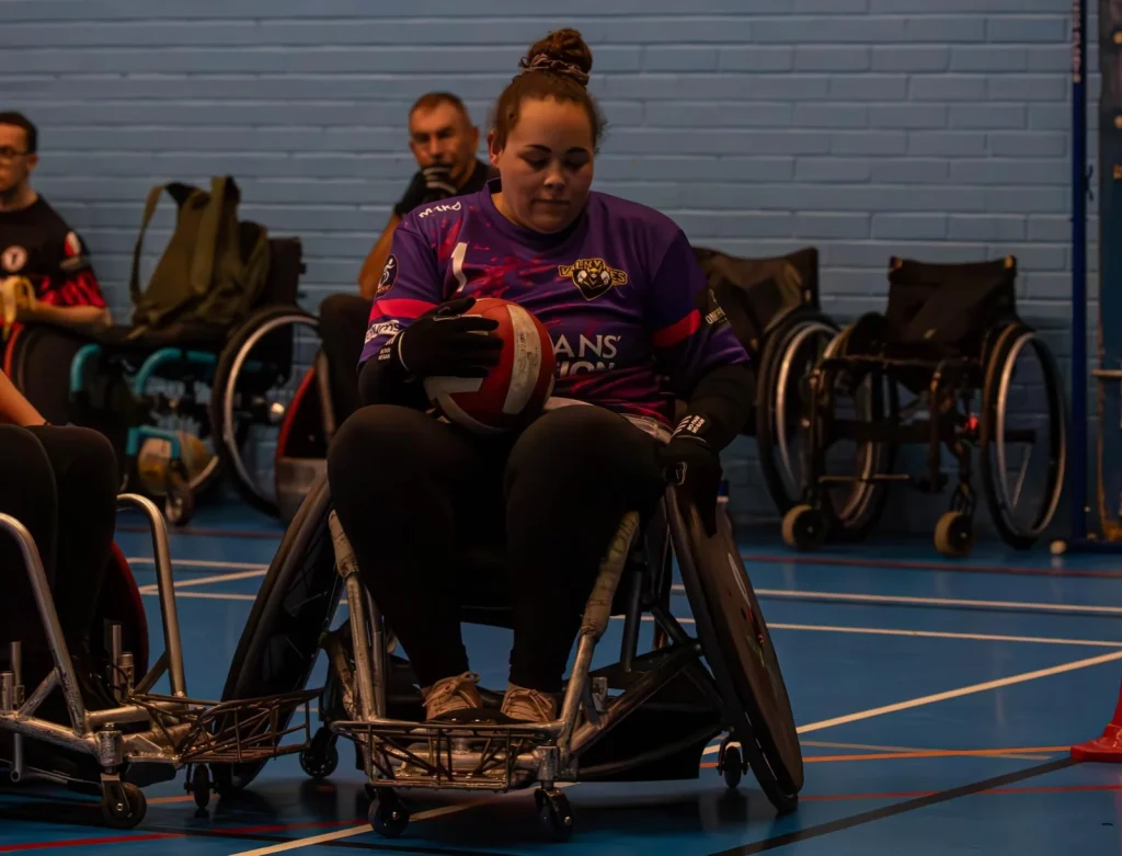 Danielle in a blue wheelchair sitting on an indoor sports court during a game.