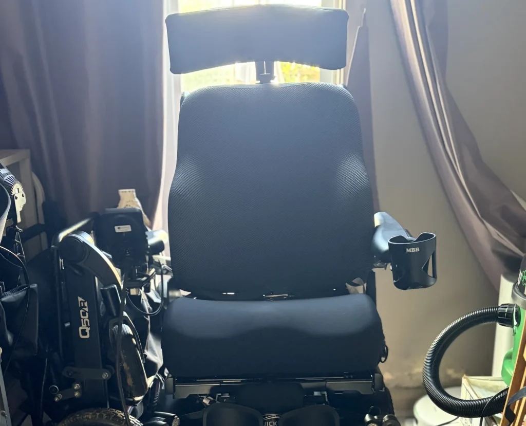 A black powered mobility chair with blue accents shown from the front in a bedroom.