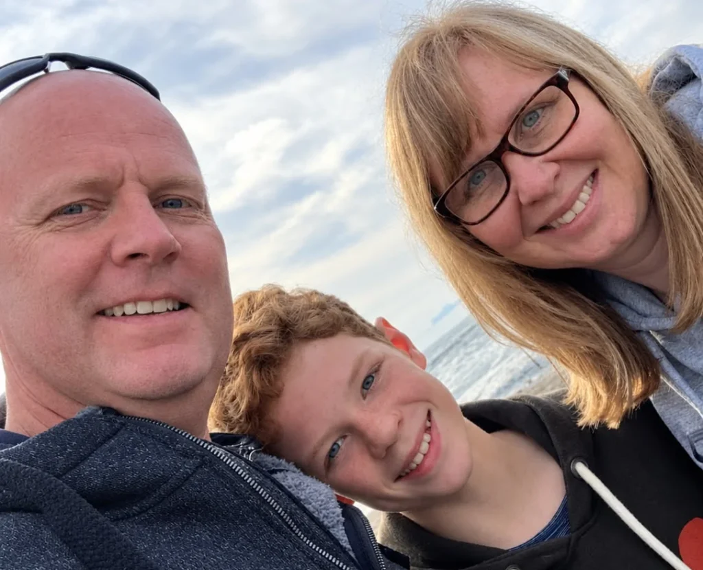 Man smiling with woman and young boy outdoors, all three happy.