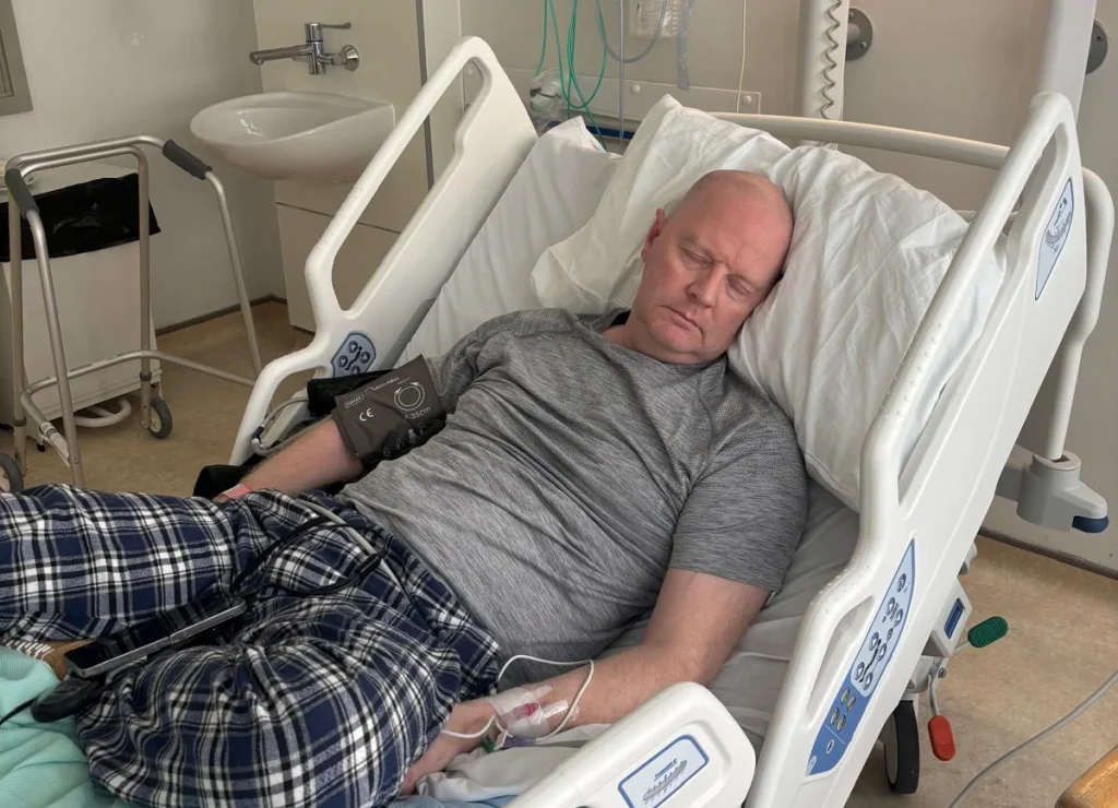 Man in hospital bed with monitoring equipment visible above.