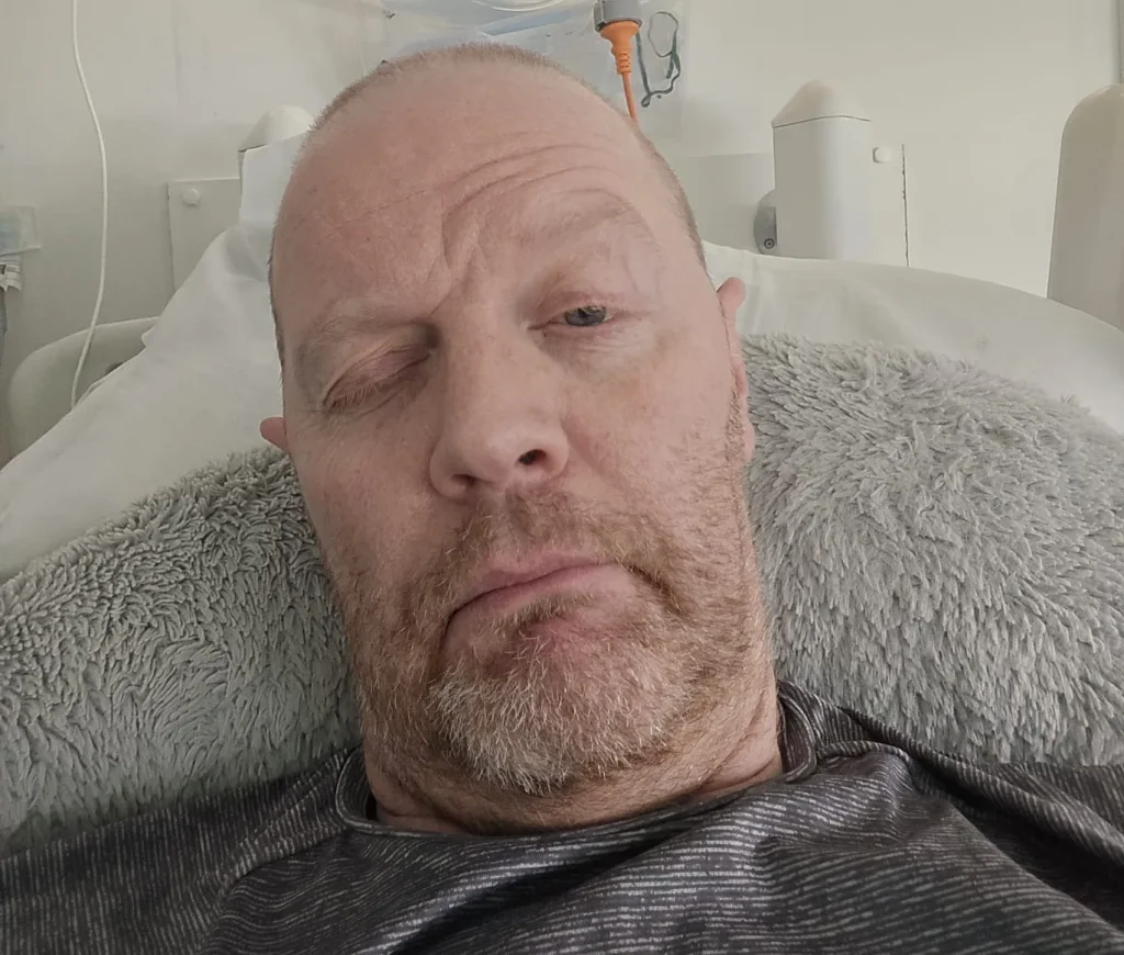 Man lying in hospital bed with IV line visible.