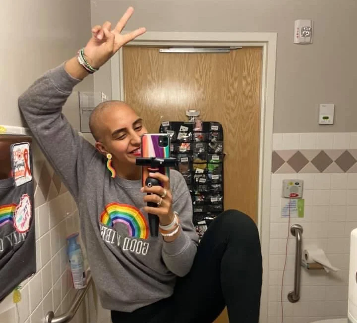 Woman holding microphone wearing rainbow sweatshirt in bathroom mirror selfie