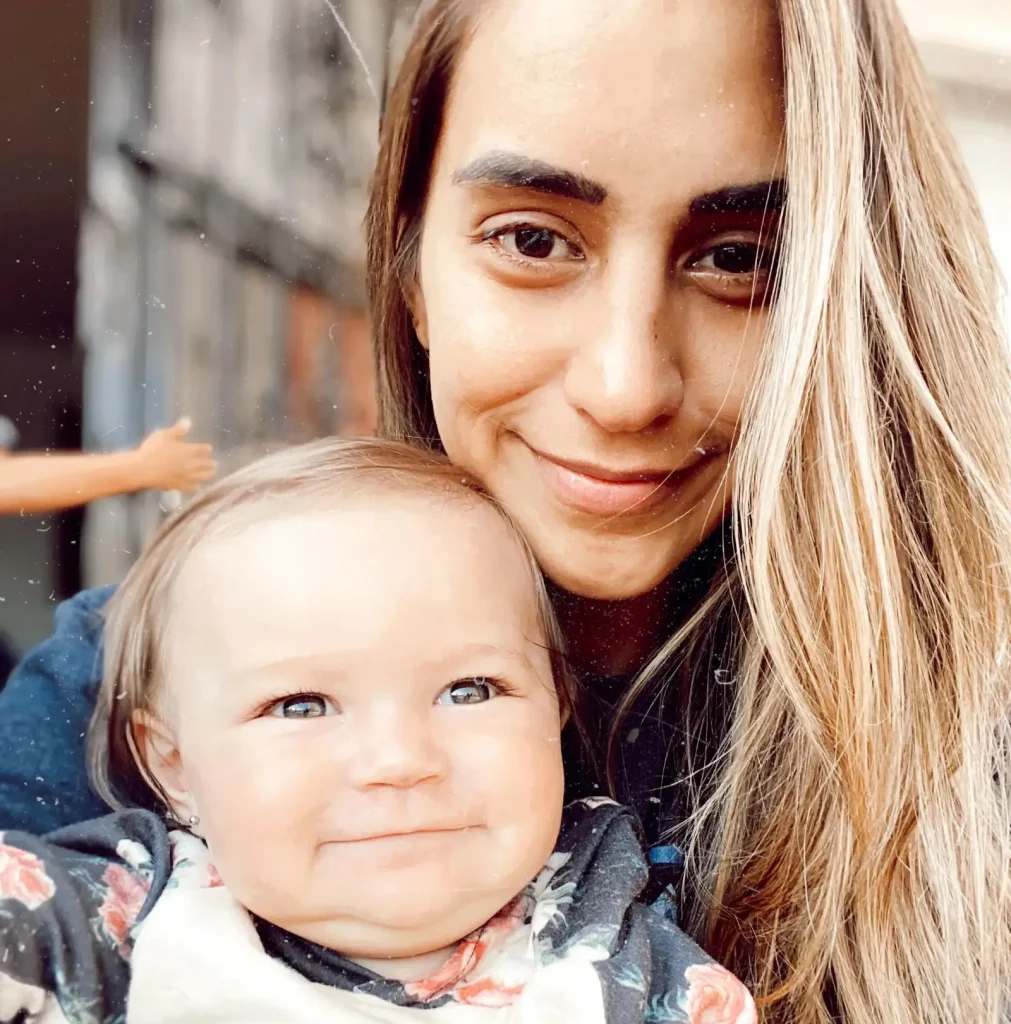 Woman with brown hair holding blonde infant, outdoor natural light portrait