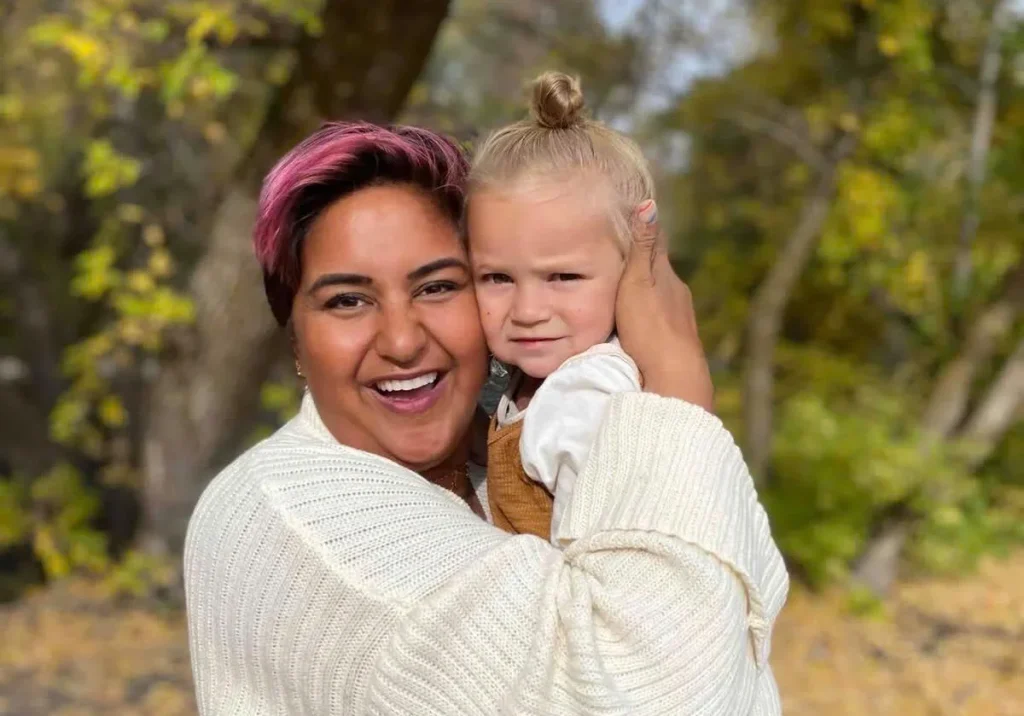 Woman with reddish hair smiling at camera holding young child outdoors