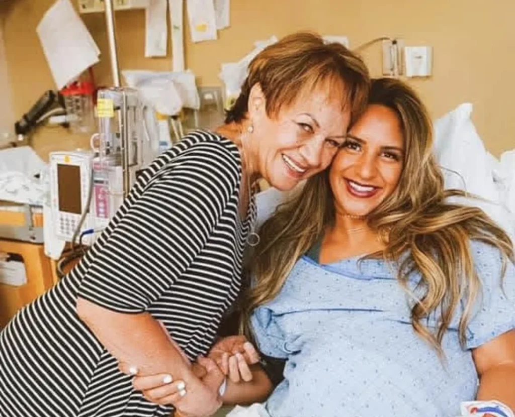 Woman in hospital bed wearing blue gown with older woman in striped shirt beside her