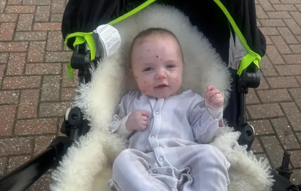 Newborn in white babygrow in black pram with lime-green handles on pavement