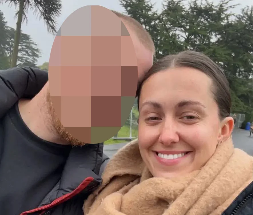 Woman in black and red jacket smiling next to man with pixelated face outdoors