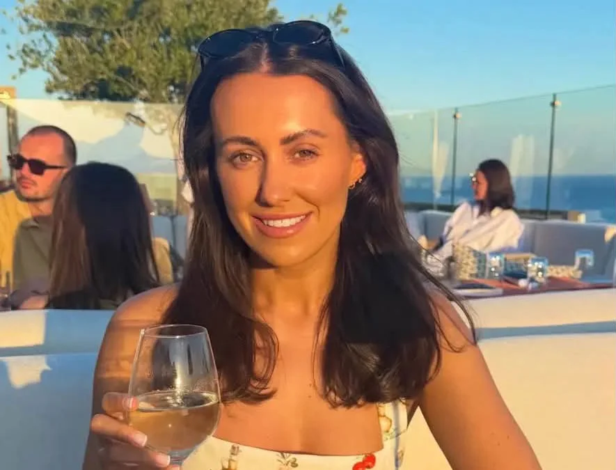 Woman in floral top holding white wine glass smiling at camera on sunny terrace