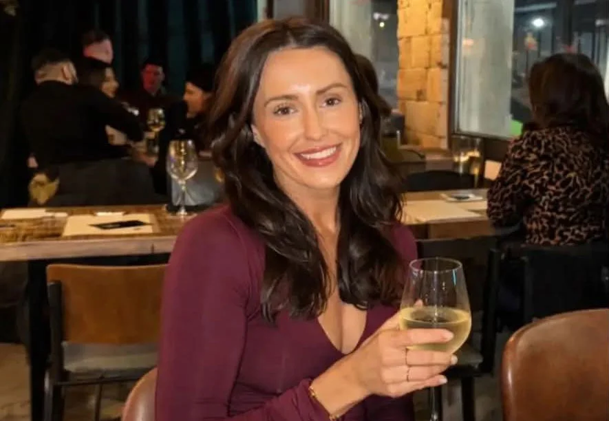 Woman with long dark hair smiling at camera in burgundy top at indoor venue