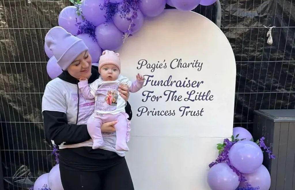 Woman and infant daughter posing outside hospital beside purple balloon fundraiser display.