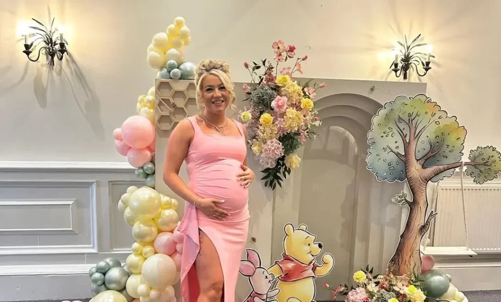 Pregnant woman in pink dress posing in front of balloon display for maternity photoshoot.