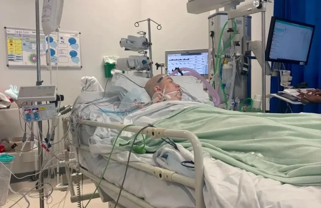 Woman lying in a hospital bed surrounded by monitors and medical equipment in an ICU setting.