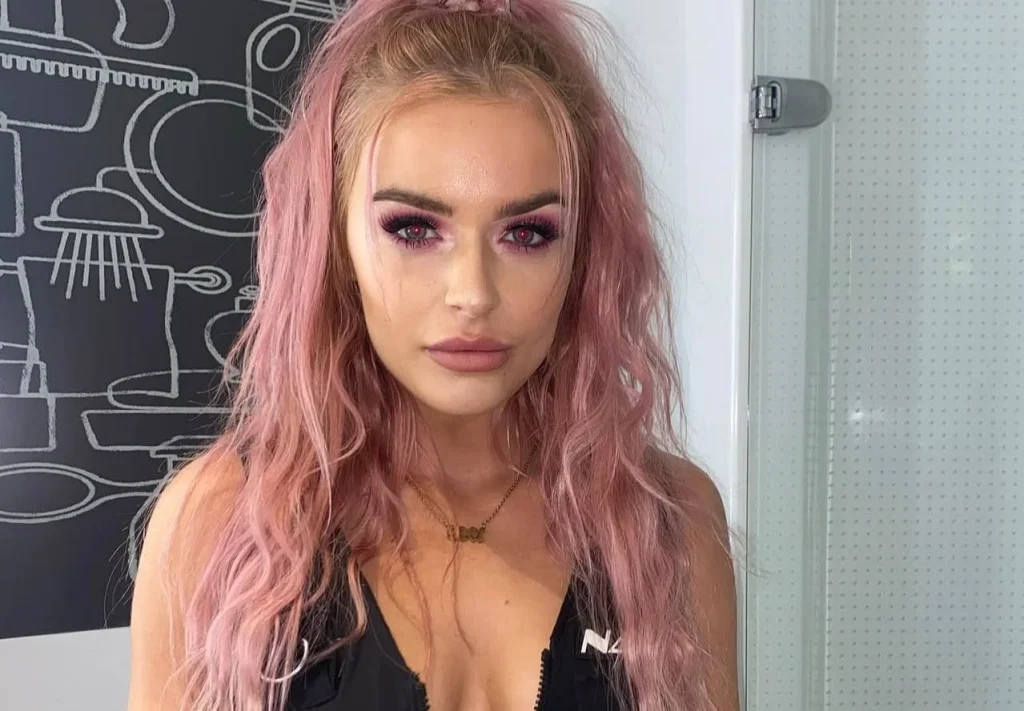 Woman with pink hair in black crop top looking directly at camera indoors.