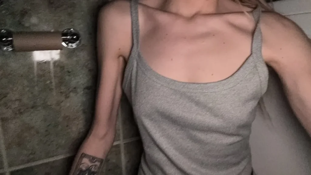 Thin woman in grey tank top with visible hip bones in bathroom.