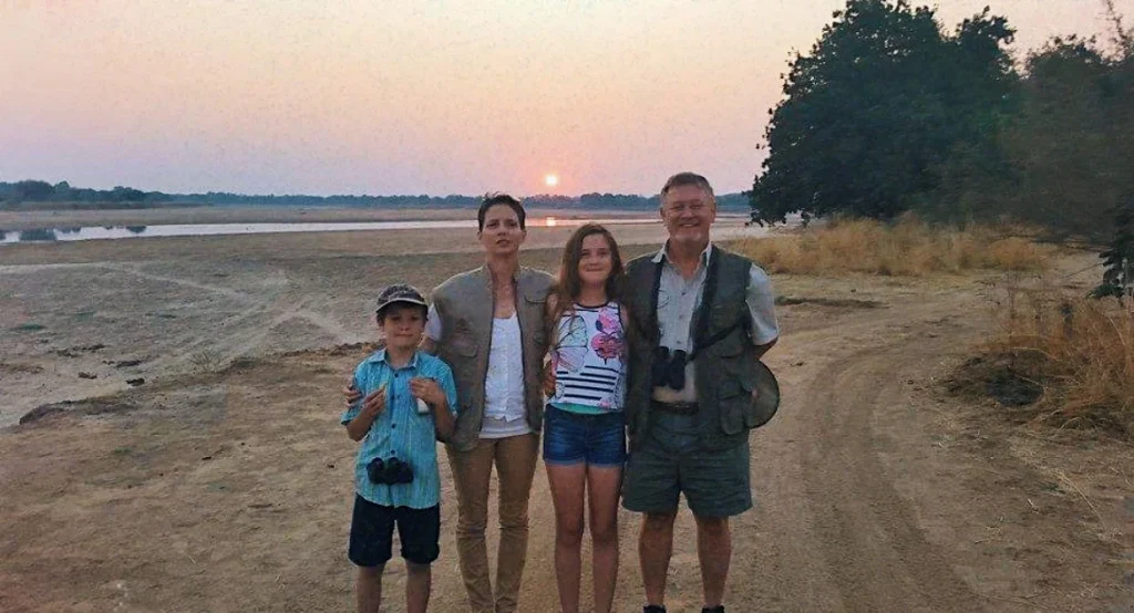 A man in khaki and a woman with two children standing together on a beach at sunset.