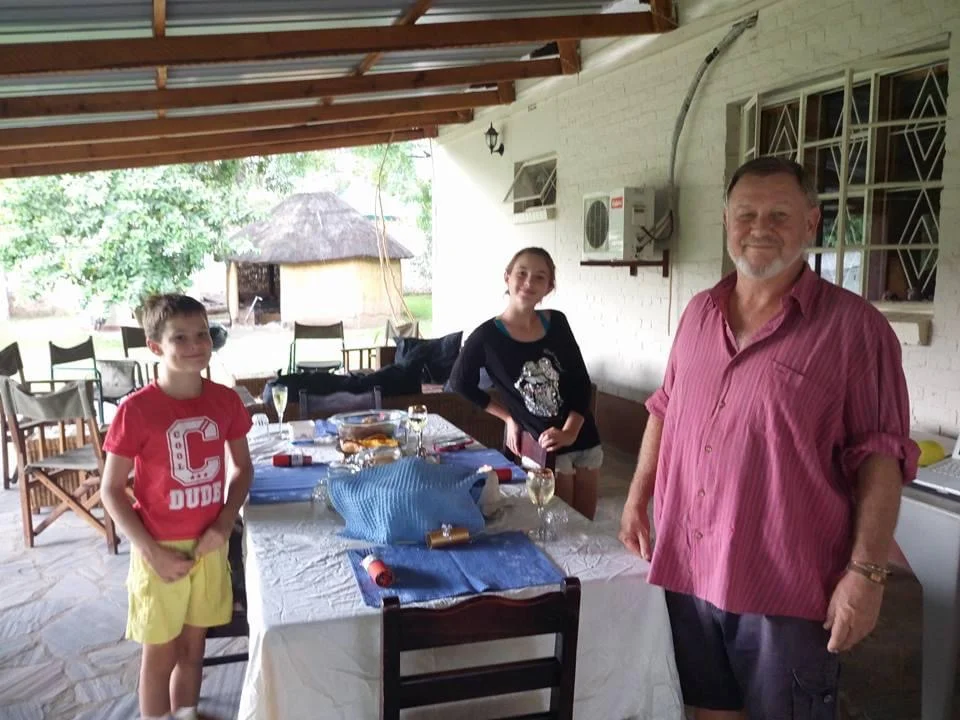 Lily, Simon and Adam in younger years standing together indoors with camping equipment.