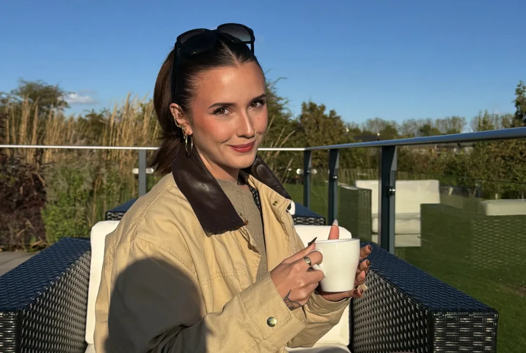 Lily Burgess, a woman with dark hair pulled back, sitting outdoors holding a cup and smiling.