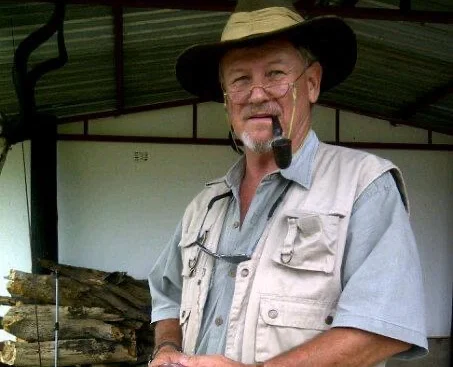 Simon, a man in light coloured shirt and khaki hat, holding a fish and smiling at camera.