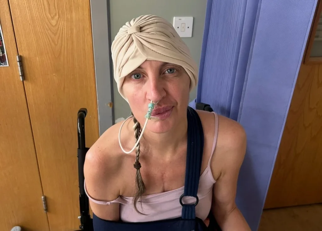 Woman wearing white head bandage and black shoulder support smiling at camera indoors.