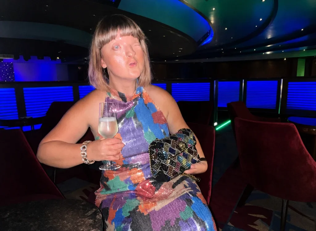 Woman in multicoloured dress holding drink on luxury boat interior.